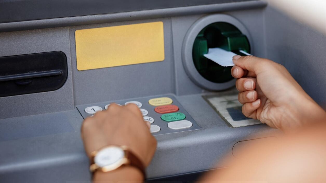 Primer plano de una mujer escribiendo el código PIN mientras retira dinero del cajero automático.