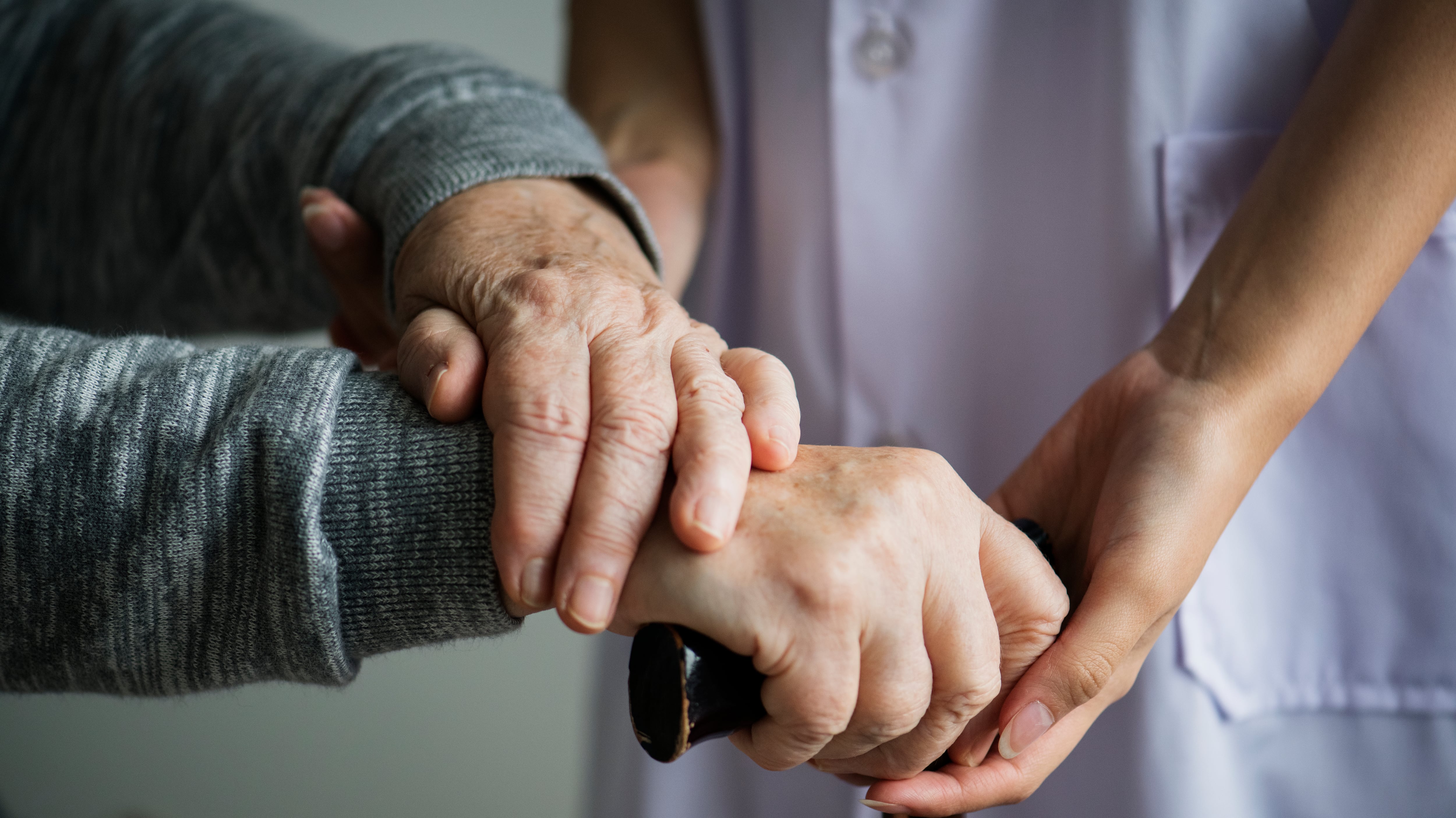 Pessoa idosa com bengala sendo ajudada por enfermeira