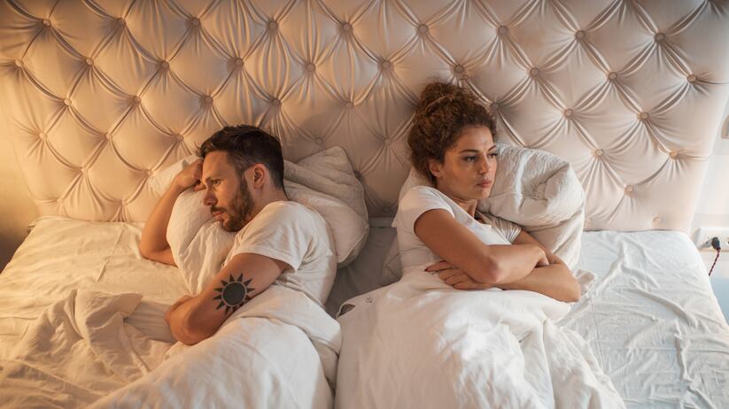 Above view of young couple lying back to back in bed while being angry at each other.