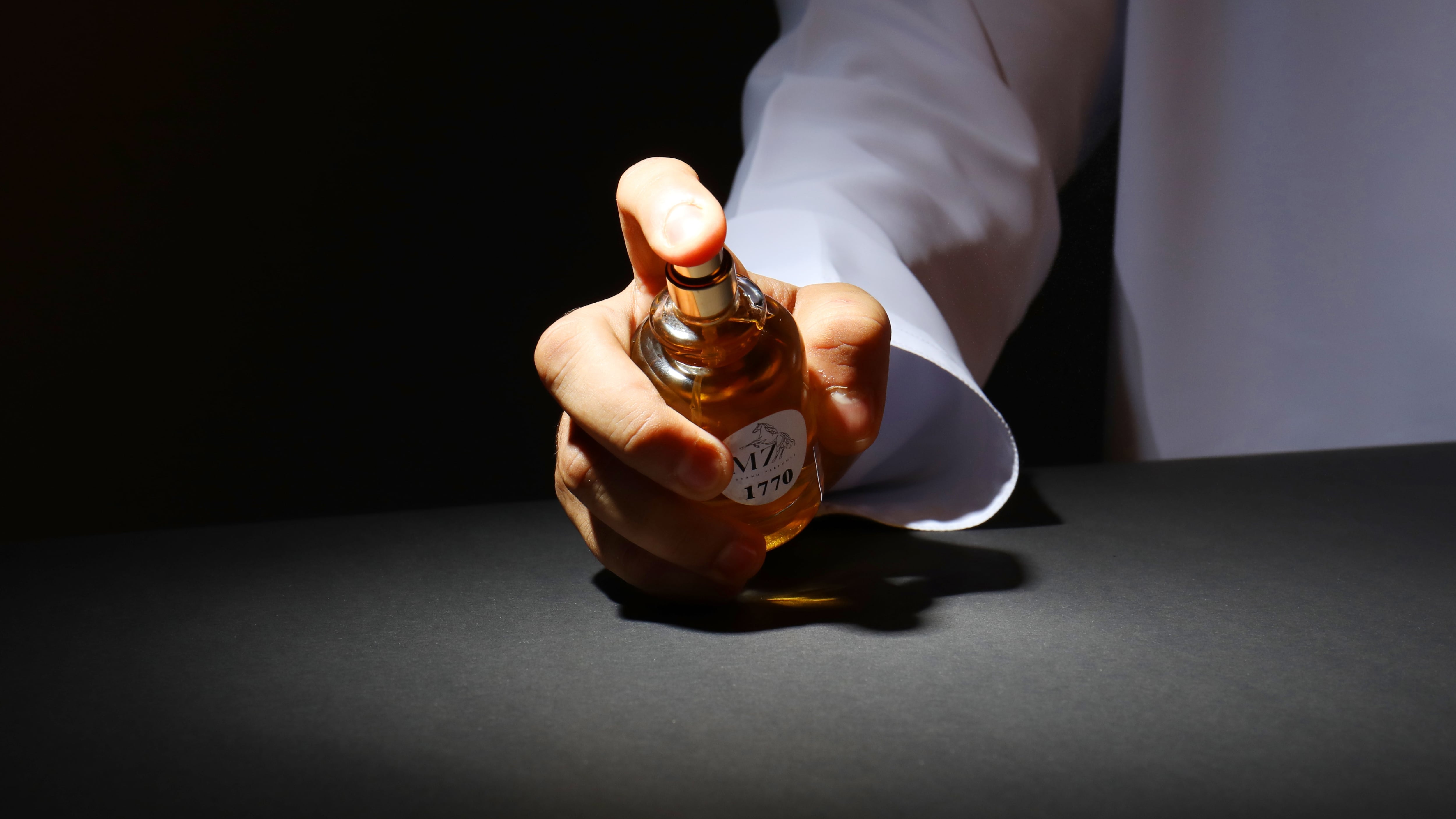 Braço masculino segurando frasco de perfume