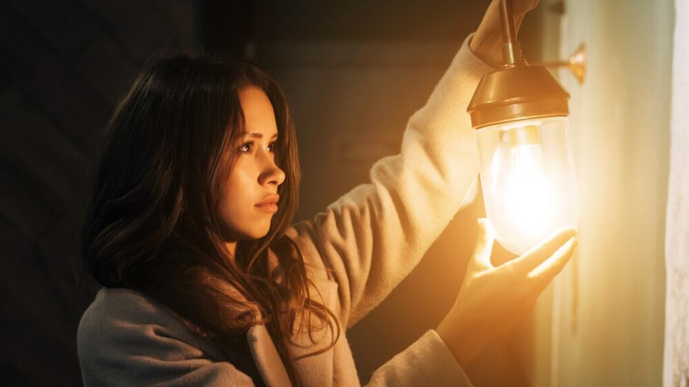 Joven hermosa mujer sostiene en su mano una pequeña lámpara de pared.